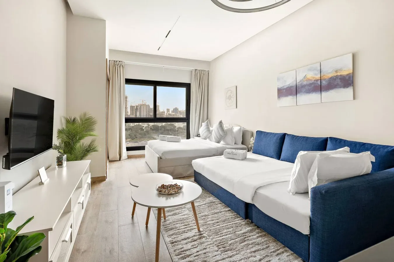 A bright living room with blue seating, a television, and a large window.