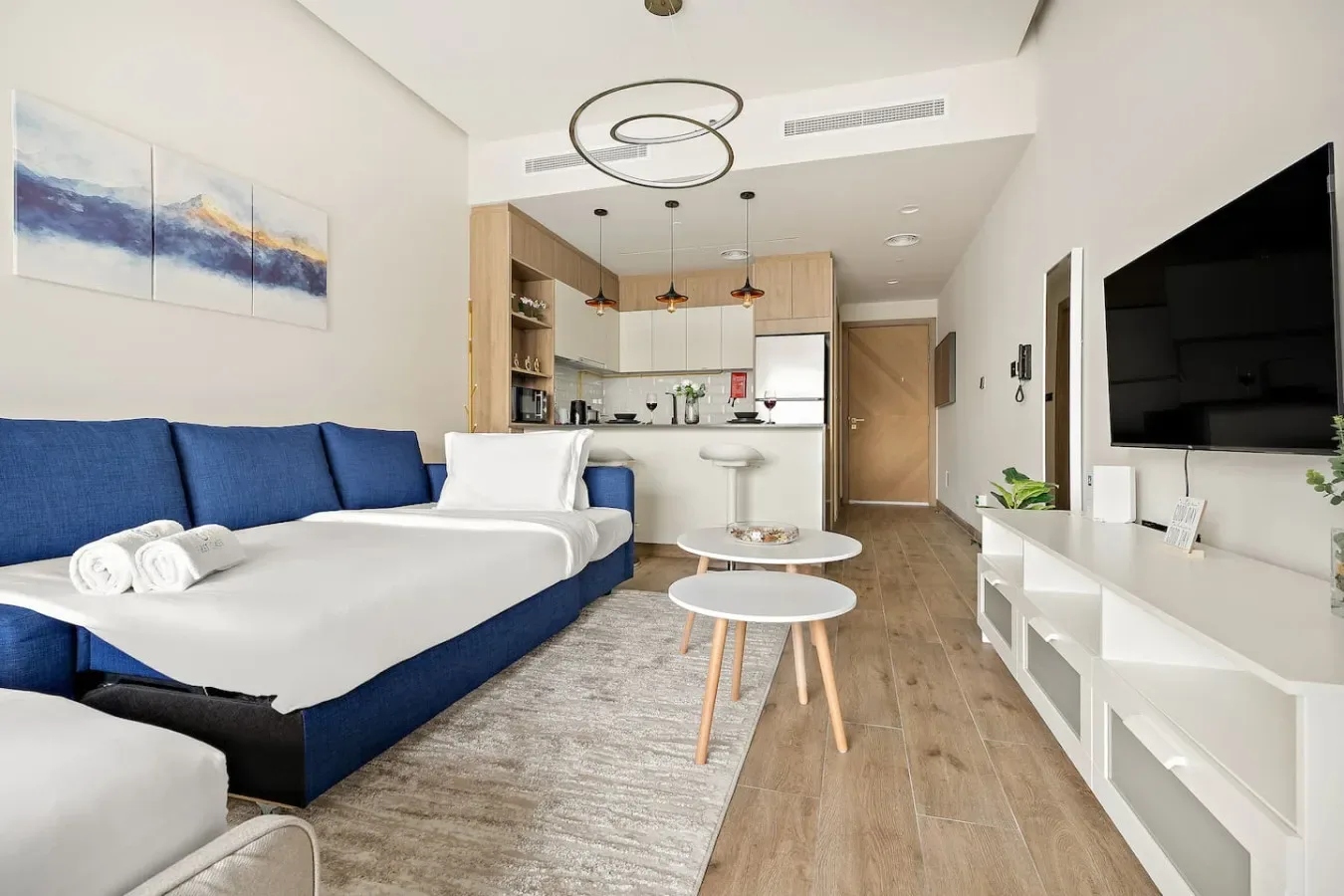 A living room with blue seating, a television, and an open kitchen.