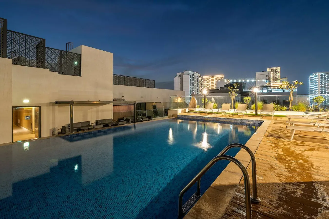 A rooftop swimming pool at night, with lounge seating along the deck.