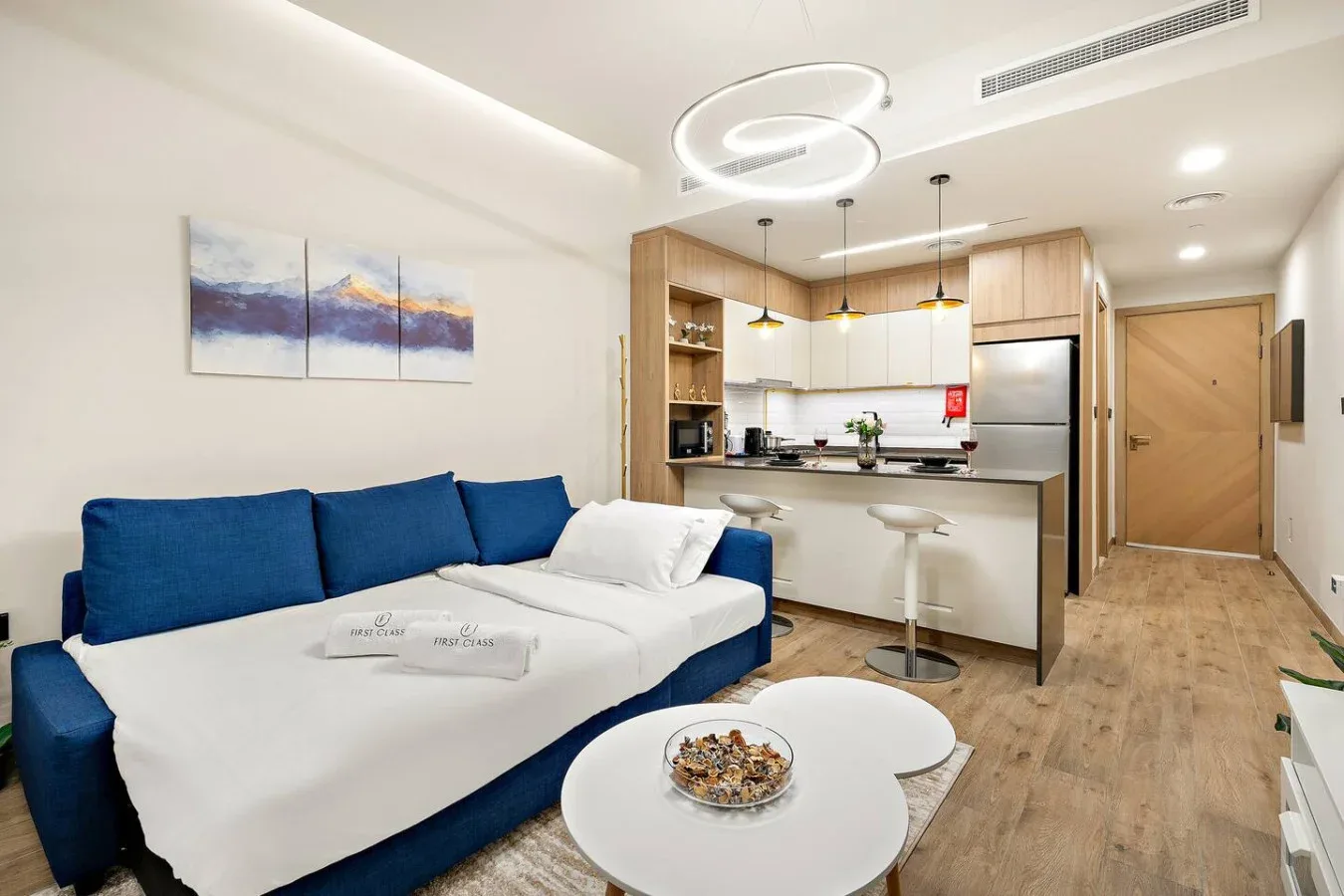 A bright living area with blue seating, a round coffee table, and an open kitchen.