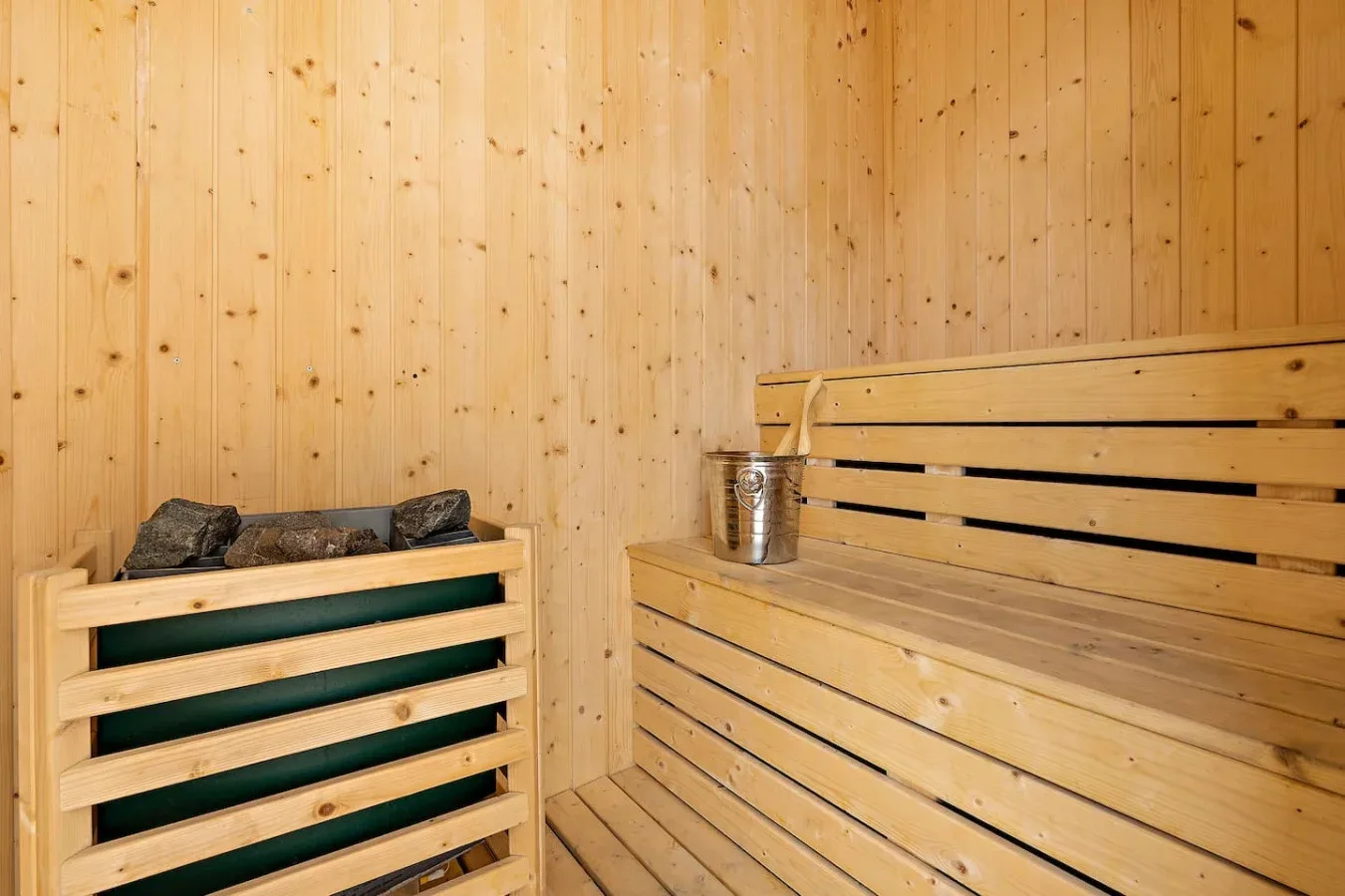 A wood-paneled sauna with tiered bench seating and a small bucket.