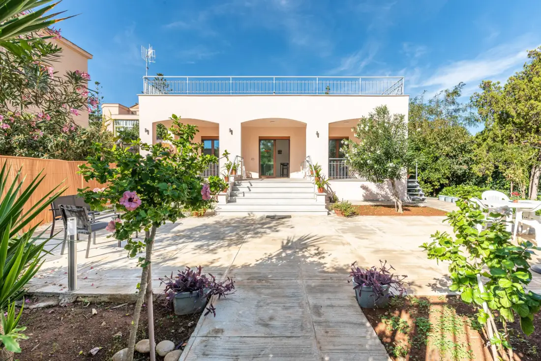 Un edificio blanco da a un patio soleado con escalones y asientos al aire libre.