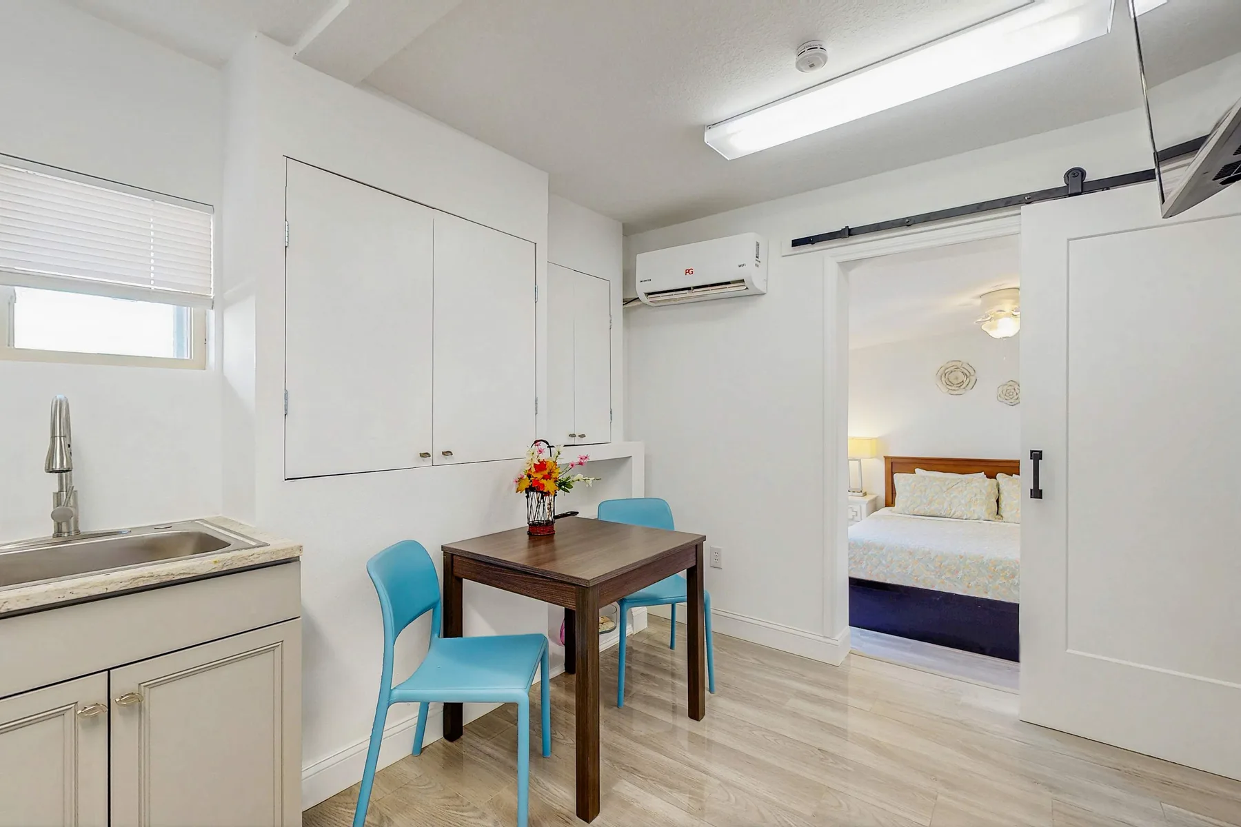 A bright kitchenette with a dining table and an open doorway to a bedroom.