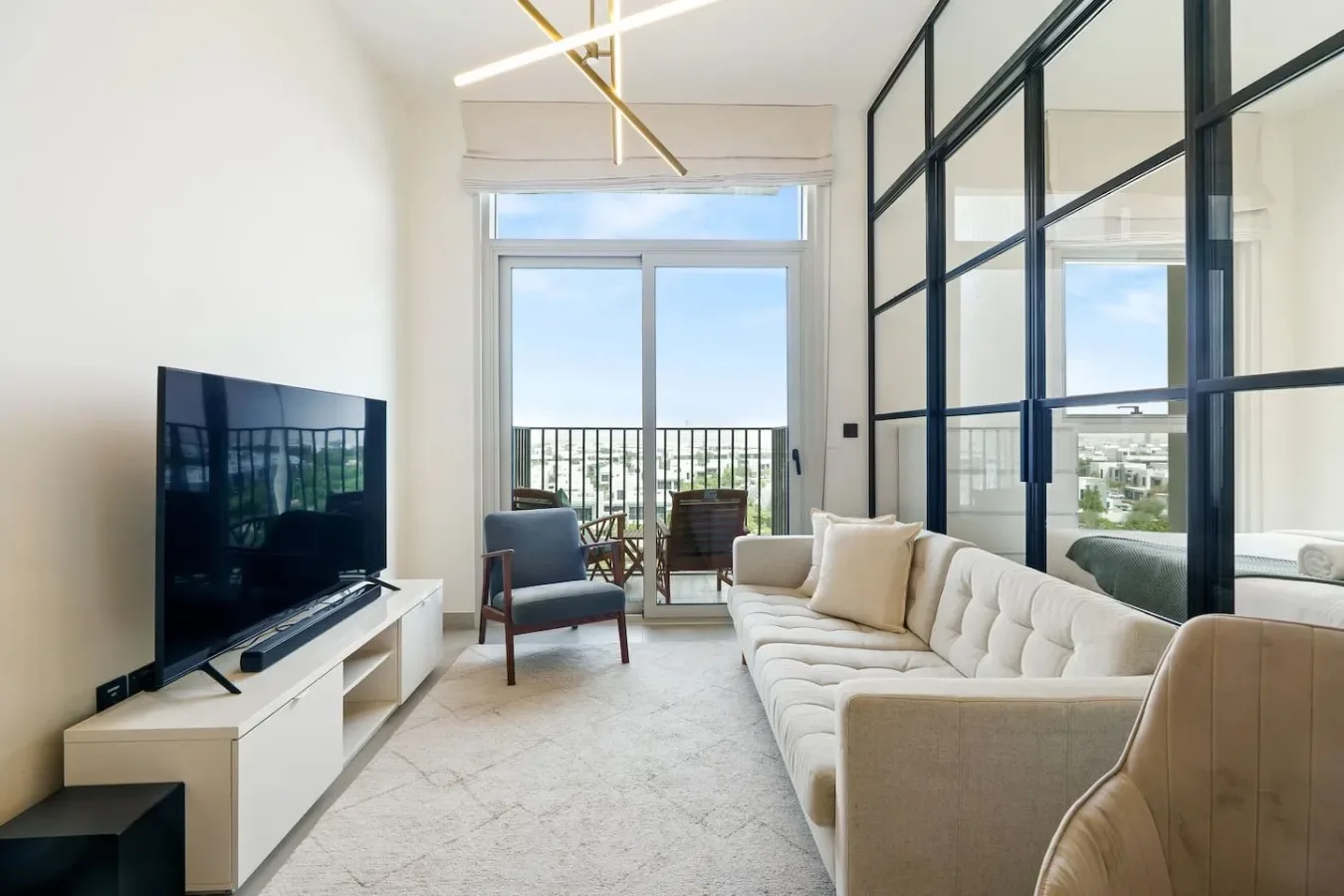 Una sala luminosa con sofá, televisor y puertas de vidrio que dan a un balcón.