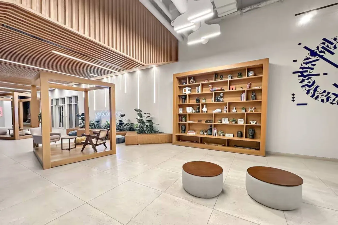 A modern lounge features a wooden display shelf and low round seating.