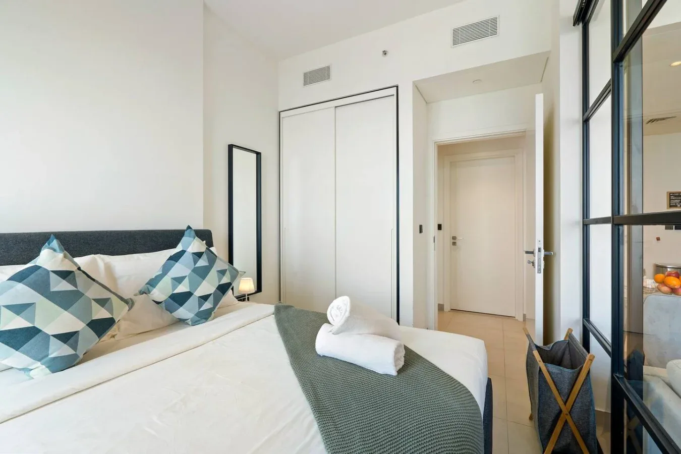 A bright bedroom with a neatly made bed and geometric-patterned pillows.