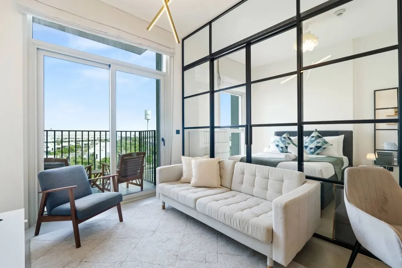 A bright bedroom and sitting area with a bed, sofa, and balcony doors.