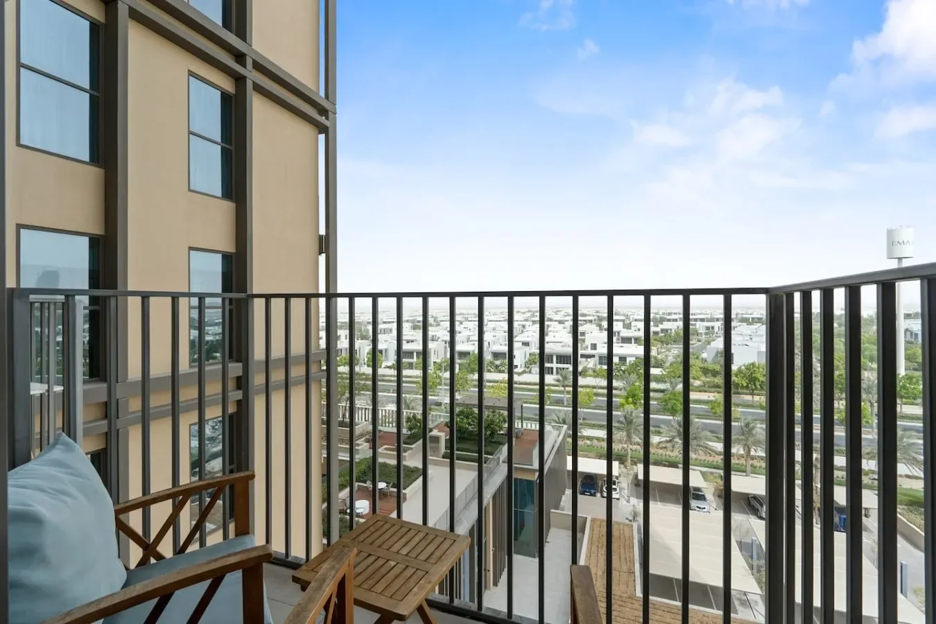 A balcony with seating overlooks a neighborhood under a blue sky.