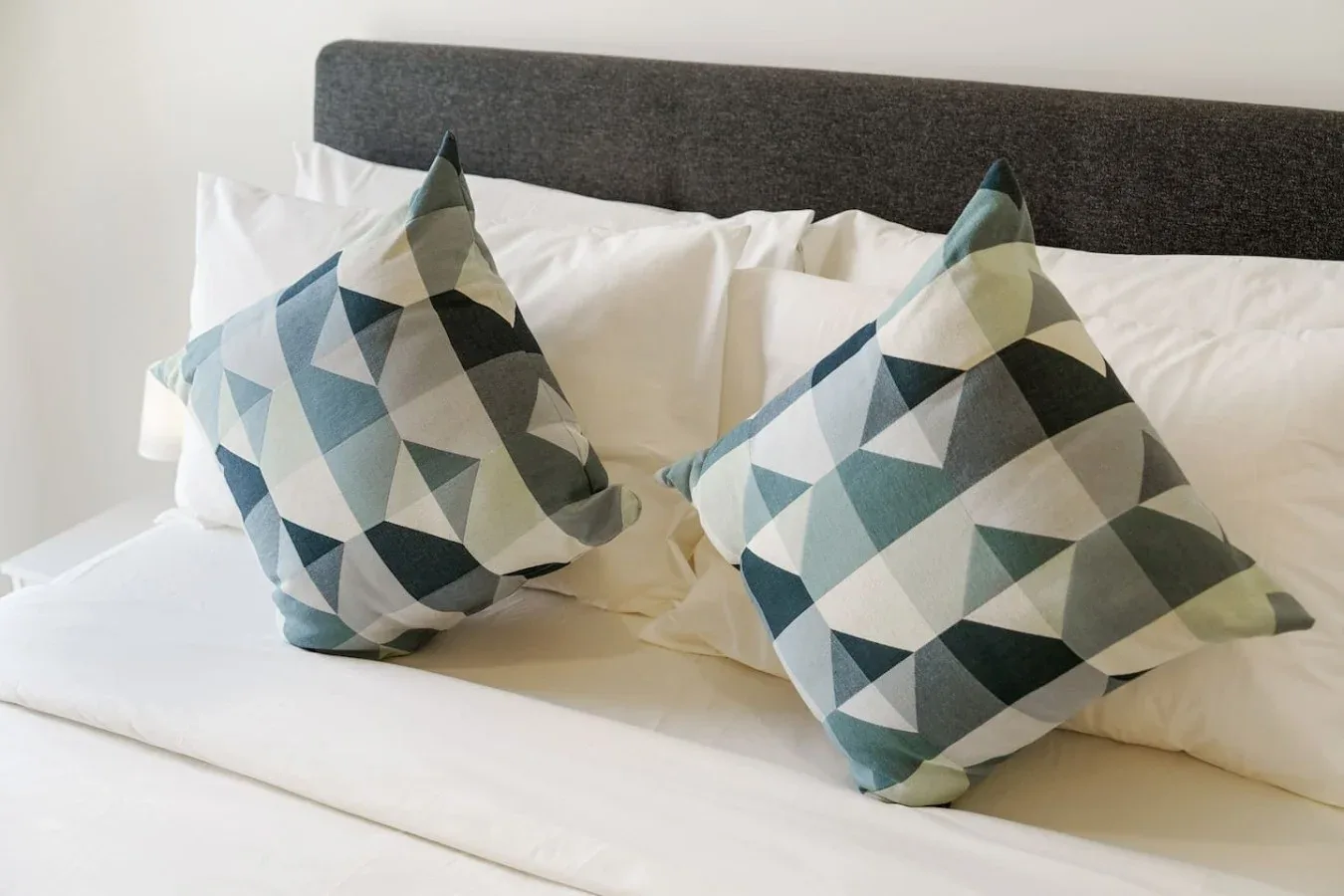 A bed with white pillows and two geometric-patterned cushions.