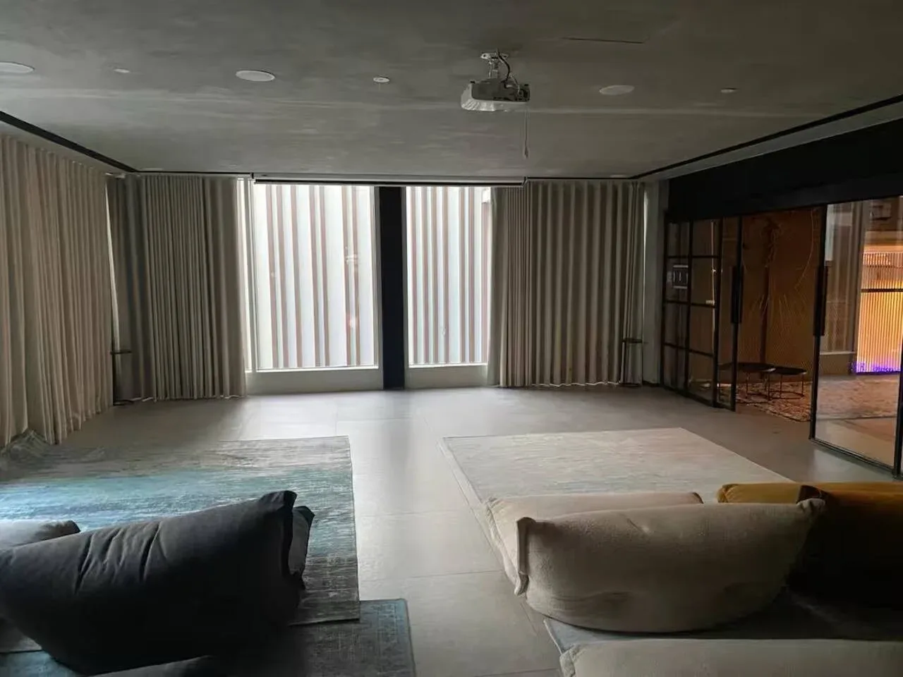 A spacious living room has seating, floor-to-ceiling curtains, and large windows.