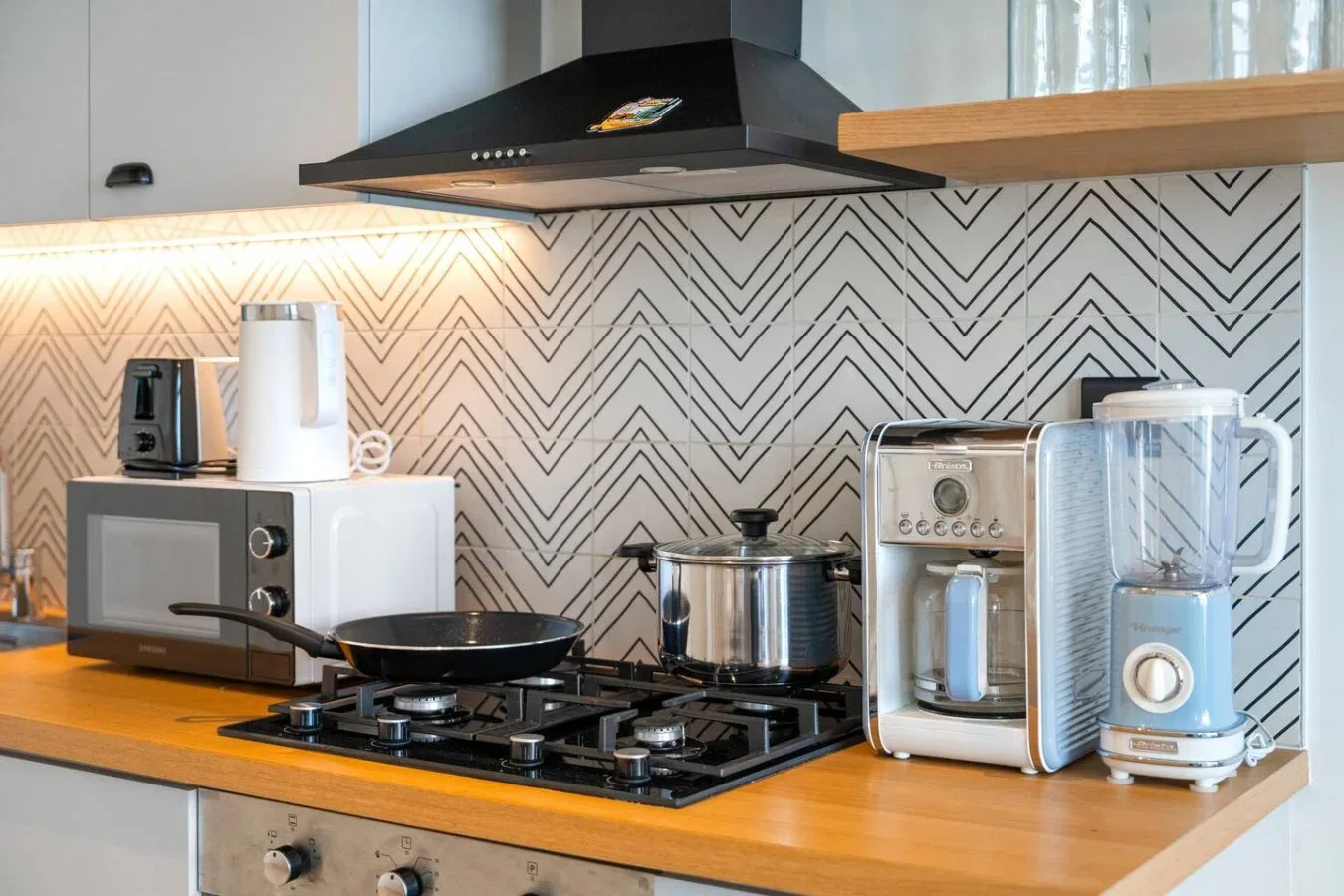 A modern kitchen counter with a cooktop, microwave, and small appliances.