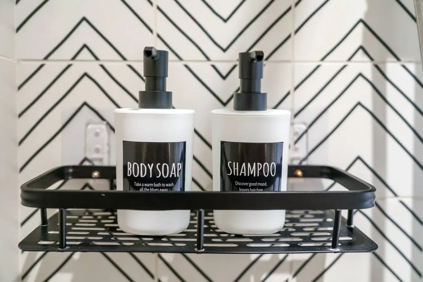 Two bottles of body soap and shampoo sit on a shelf against patterned bathroom tile.