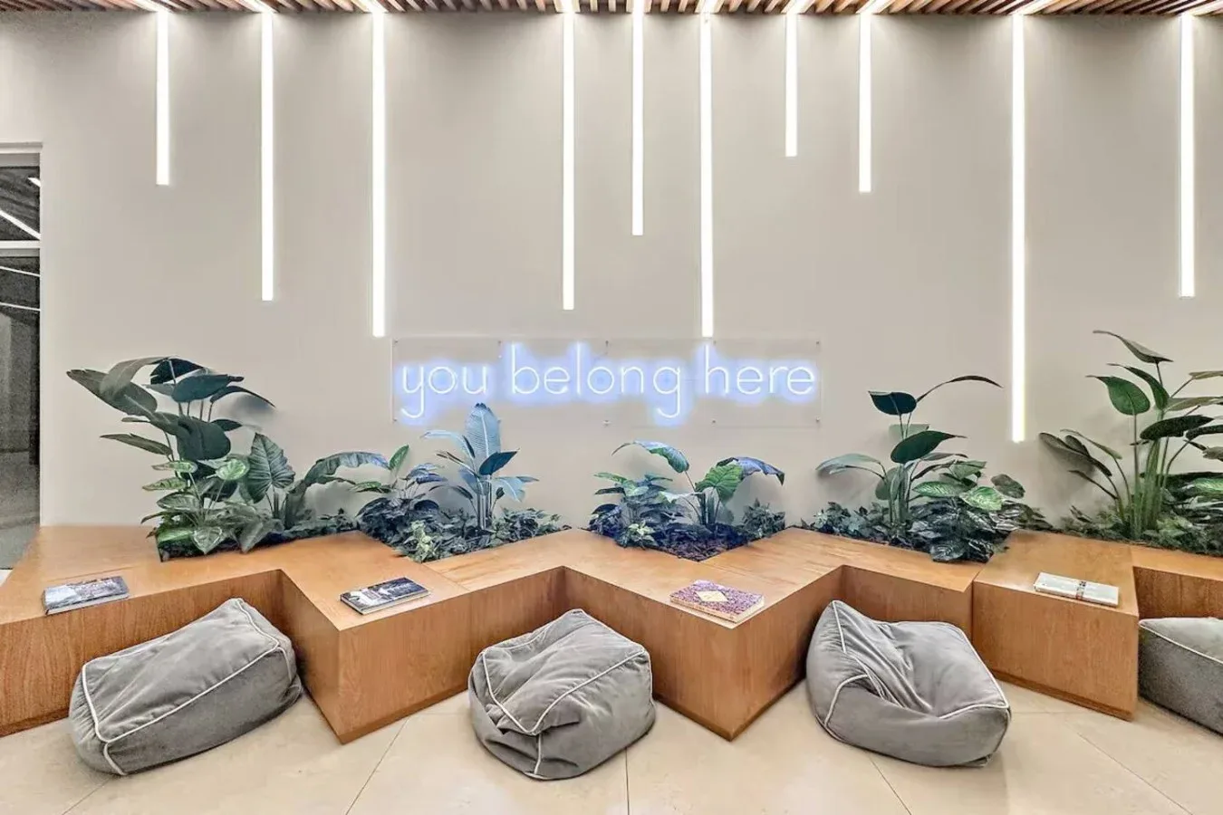 A lounge seating area with floor cushions and plants beneath a glowing wall sign.