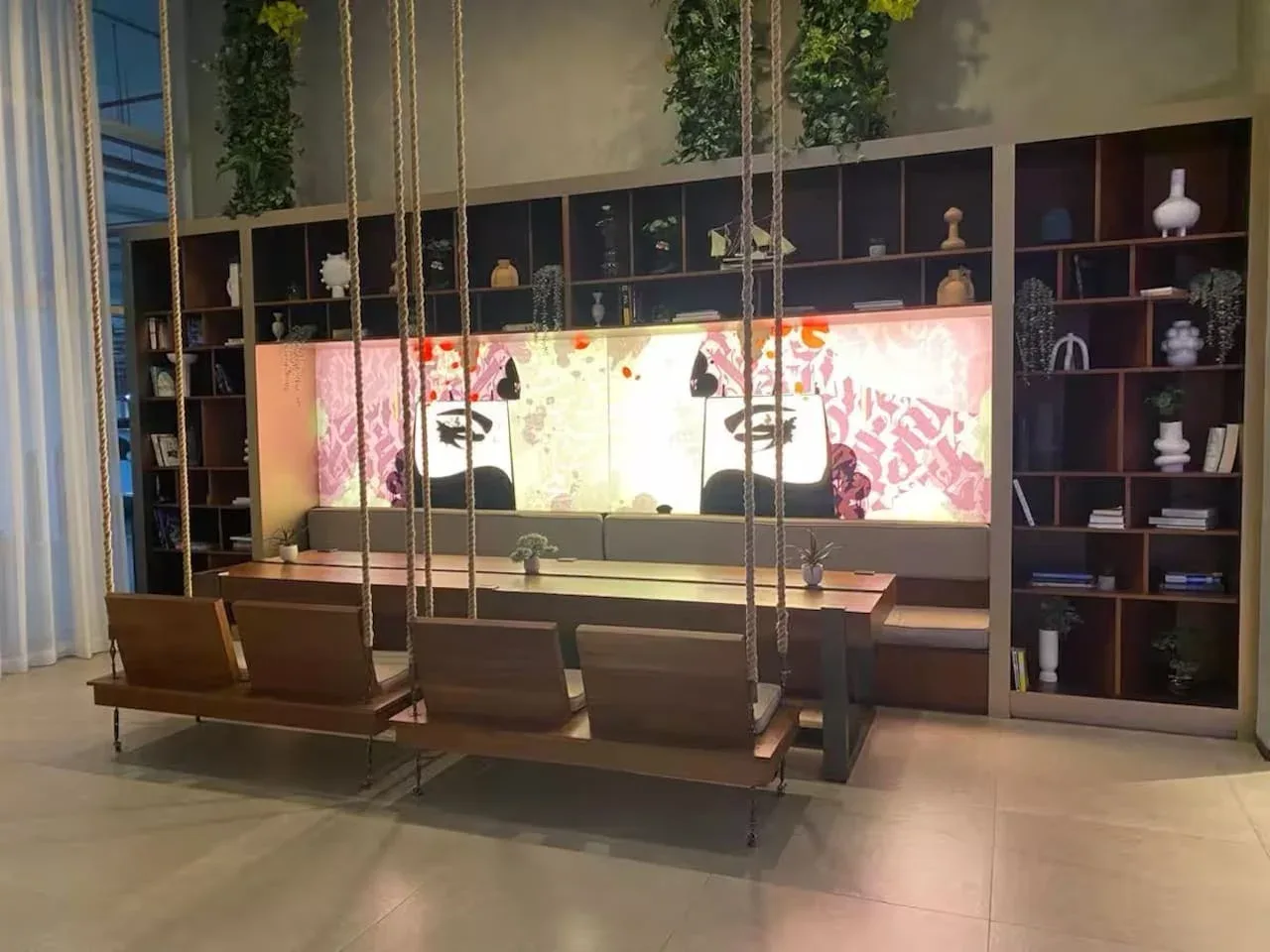 A lounge seating area faces a long shelving wall and illuminated artwork.