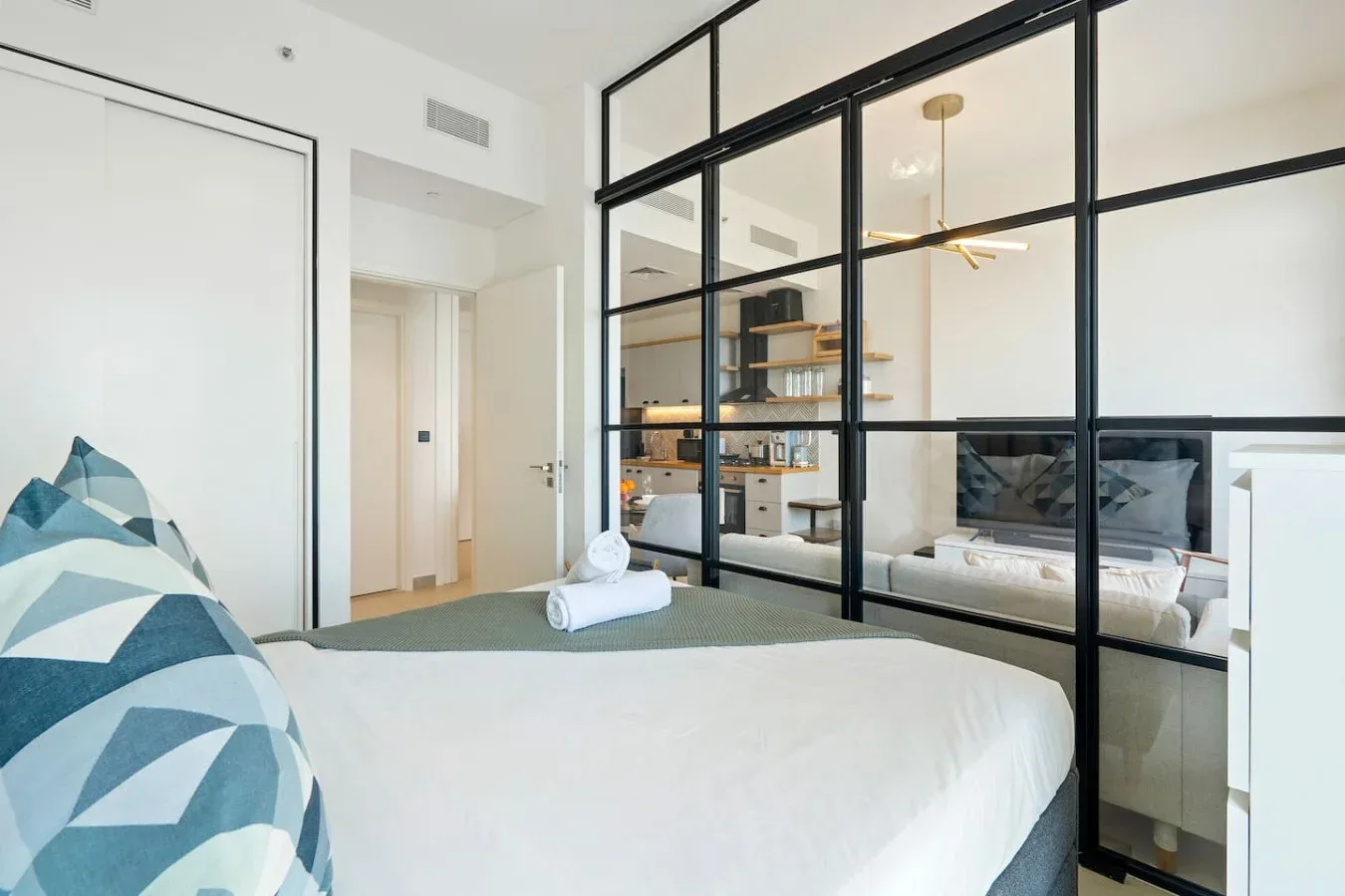 A bedroom with a bed beside a black-framed glass partition.