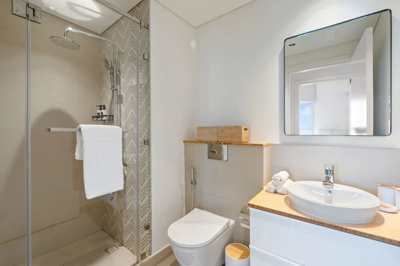 A bright bathroom with a glass shower, toilet, and sink beneath a large mirror.