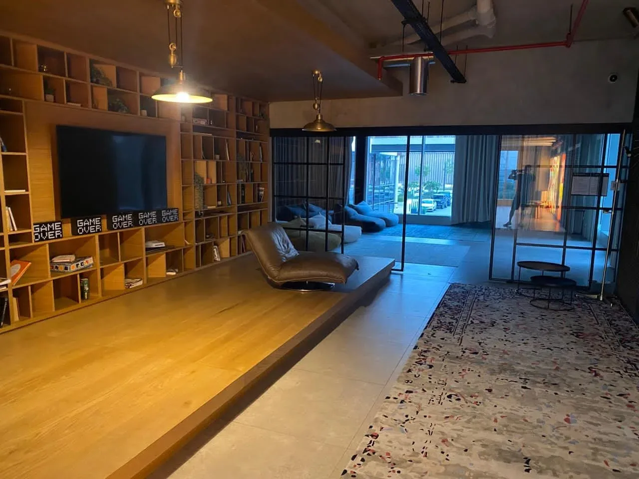 A spacious living room with built-in shelving, seating, and glass doors opening to a balcony.
