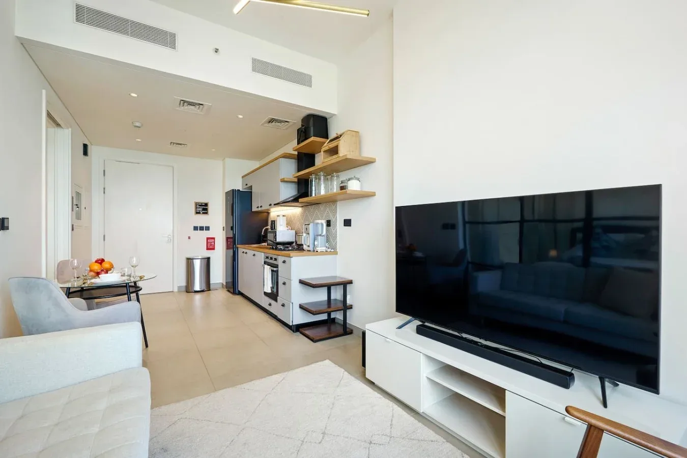A bright living area with seating, a television, and an open kitchen.