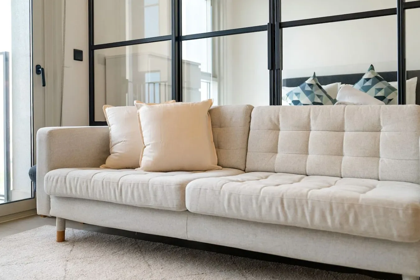 A bright living room with a large beige sofa and patterned cushions.