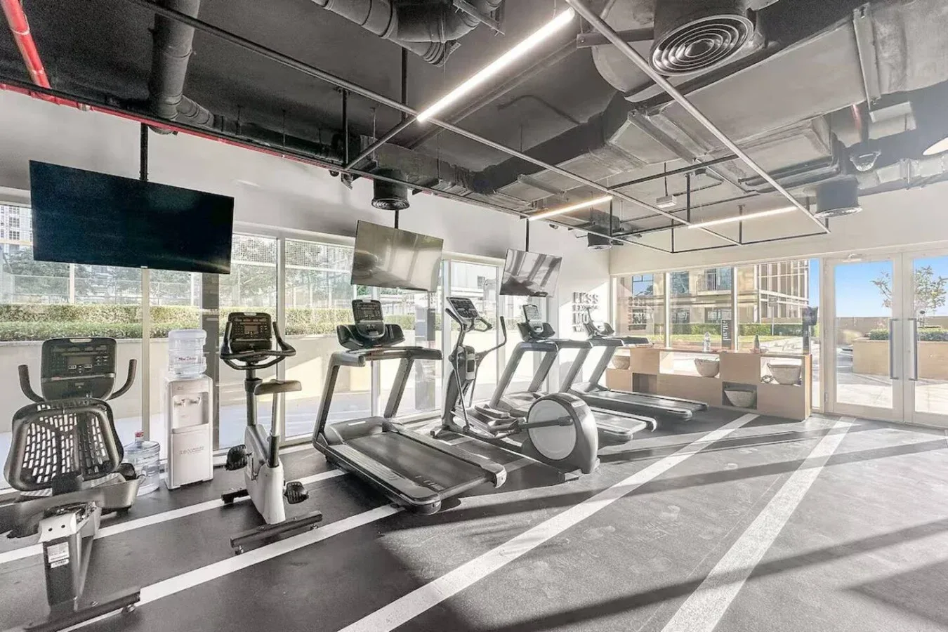 A gym with treadmills and exercise bikes beside large windows.
