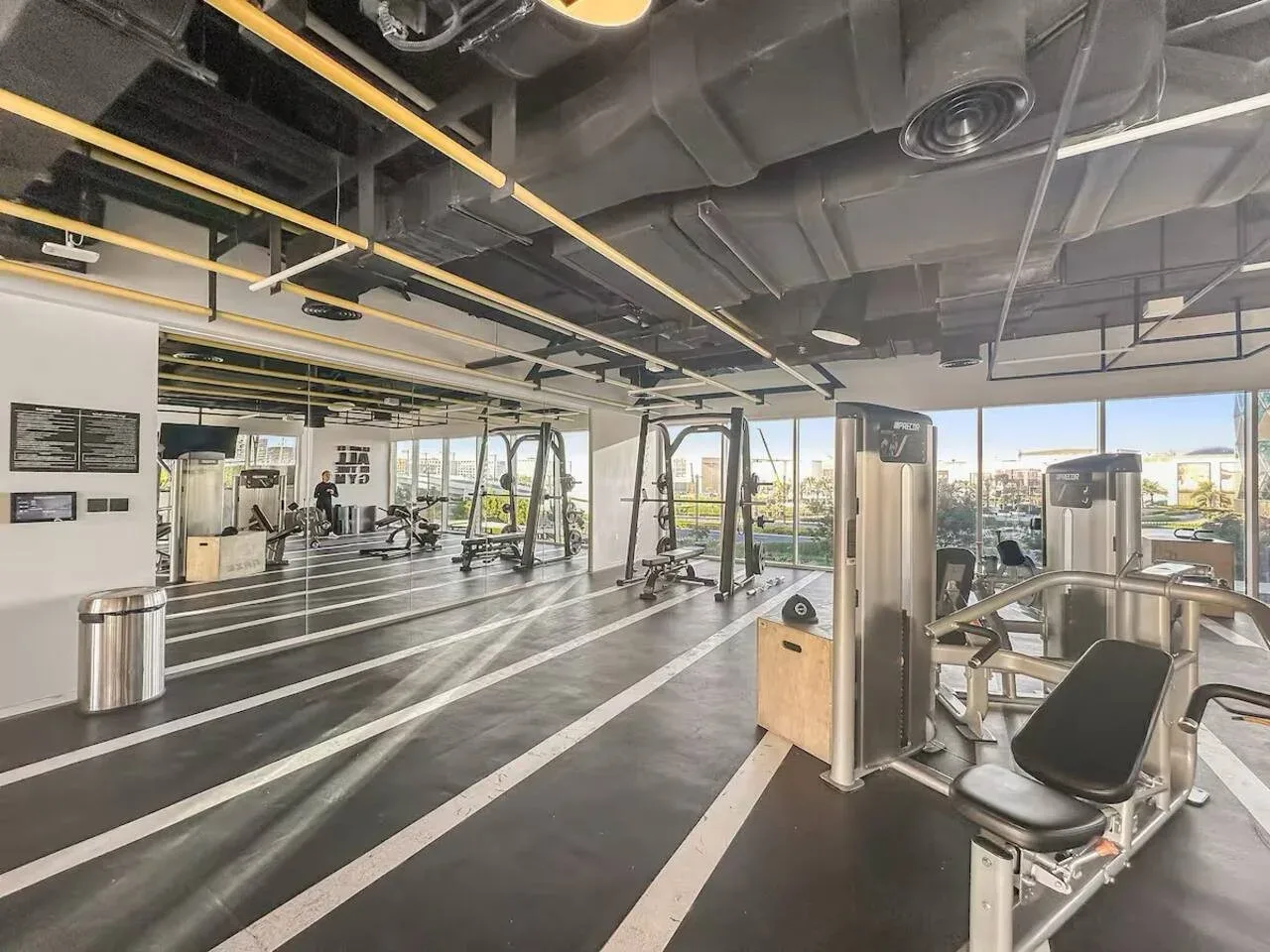 A gym with exercise machines and large windows overlooking the city.