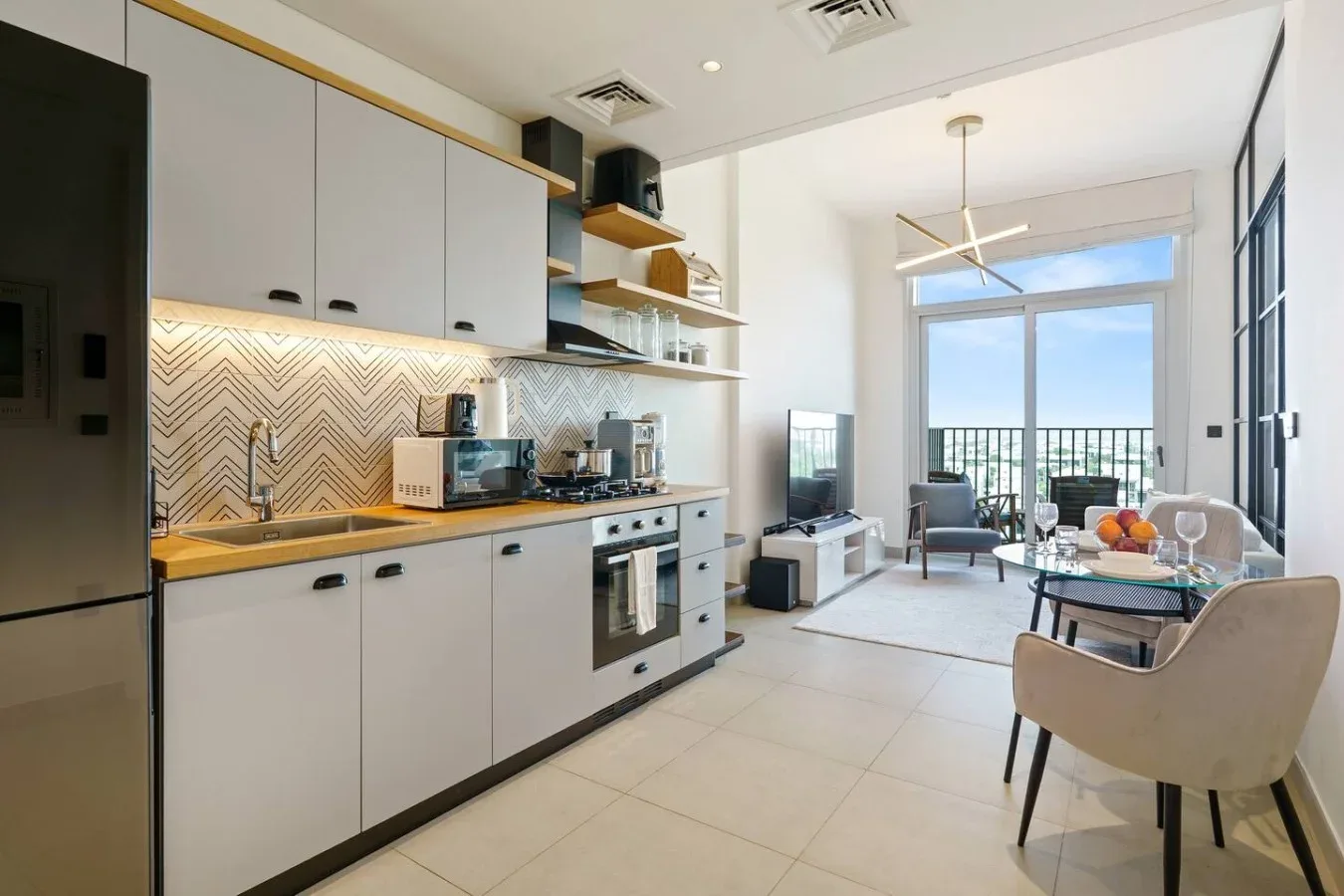 A bright open-plan kitchen and dining area with large windows and a glass table.