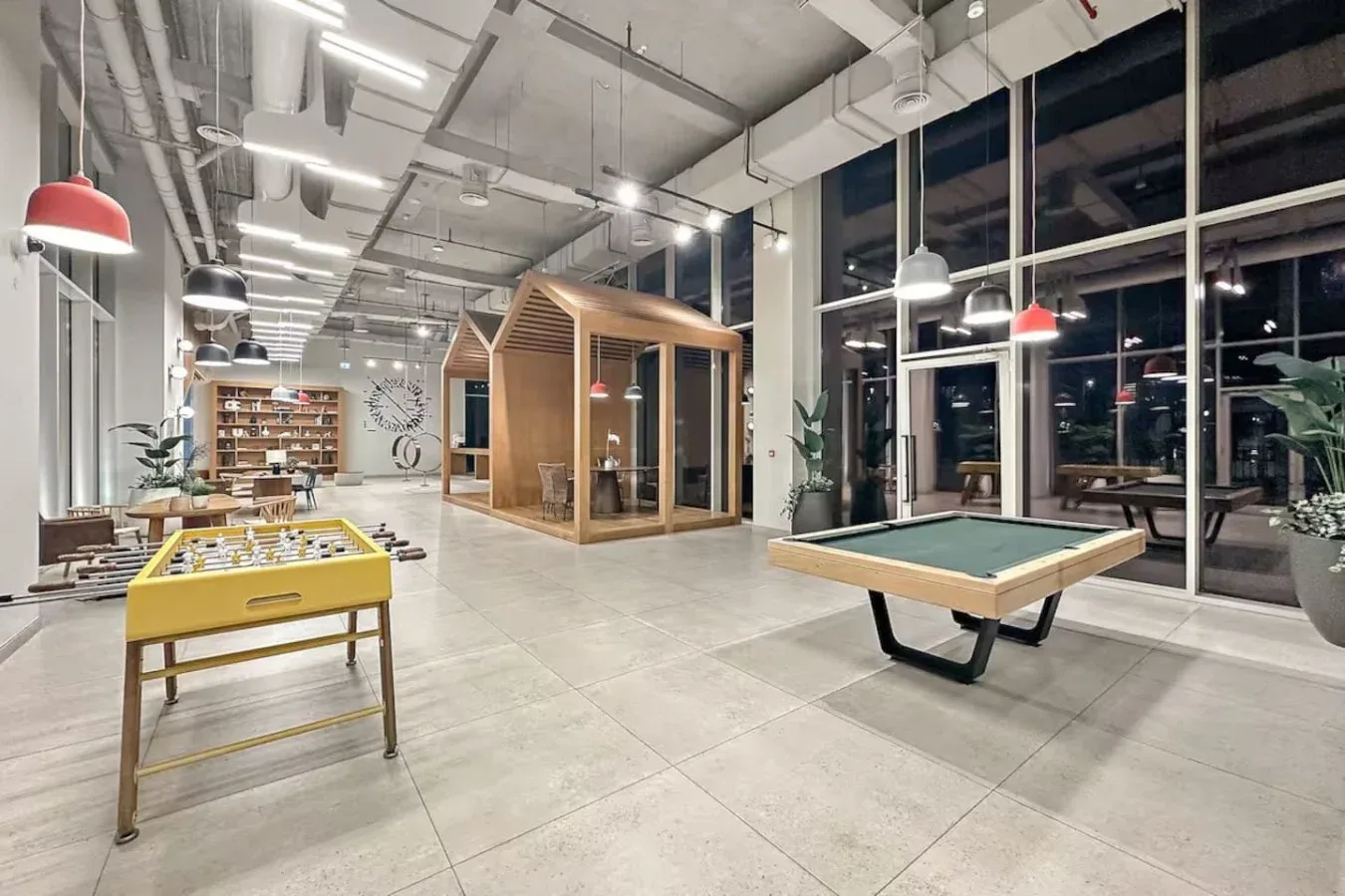 A recreation room with a pool table and foosball table beside floor-to-ceiling windows.
