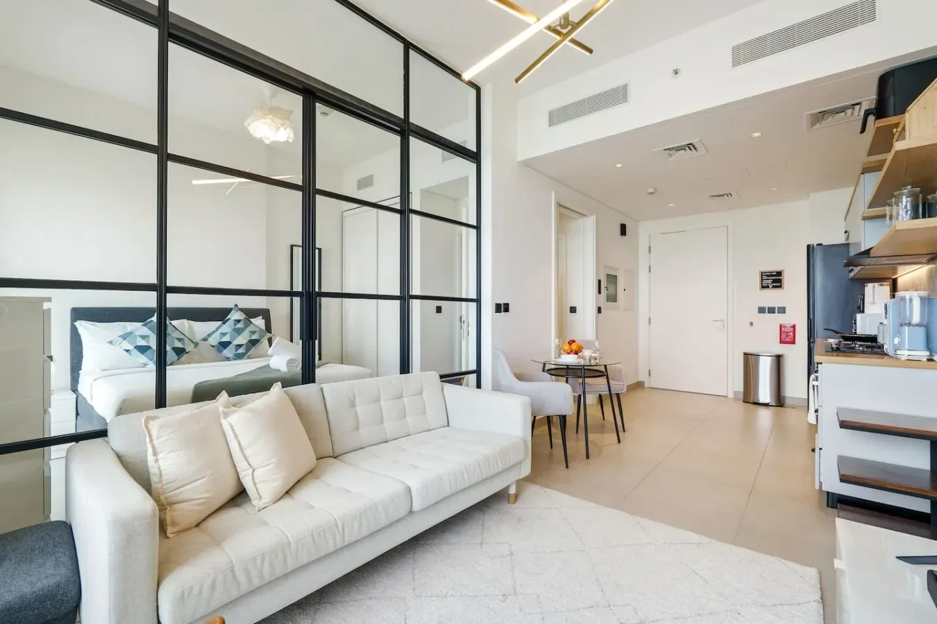 A bright living area with a light sofa and a glass-partitioned sleeping space.