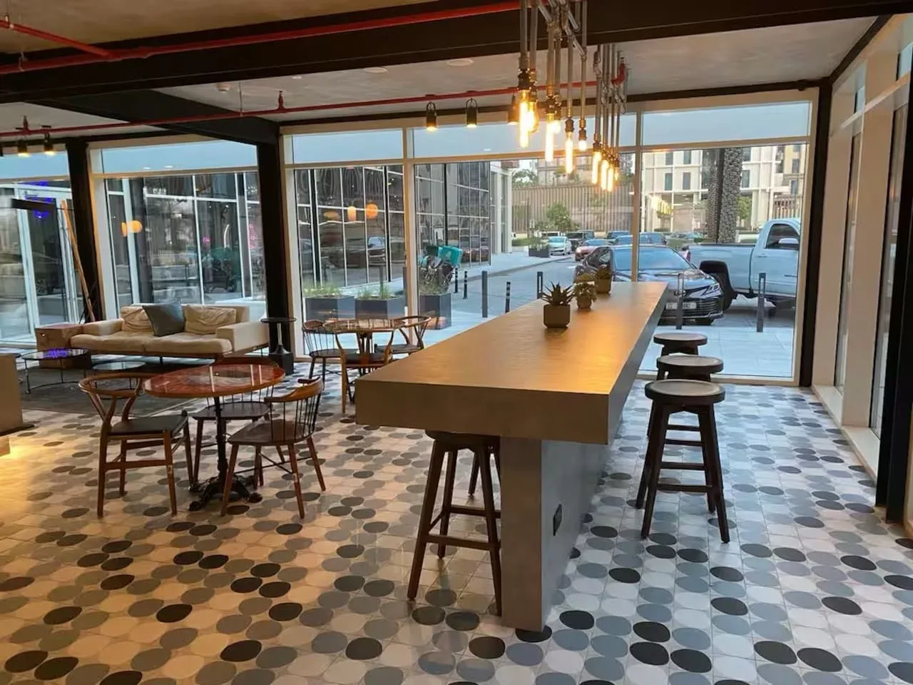 A café seating area with a long counter, stools, tables, and large windows.