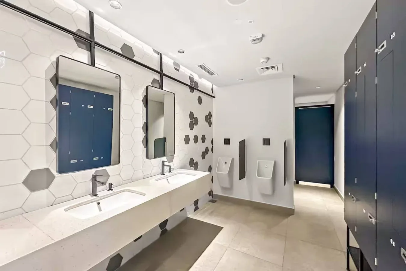 A modern restroom with a long sink counter, wall mirrors, and urinals.