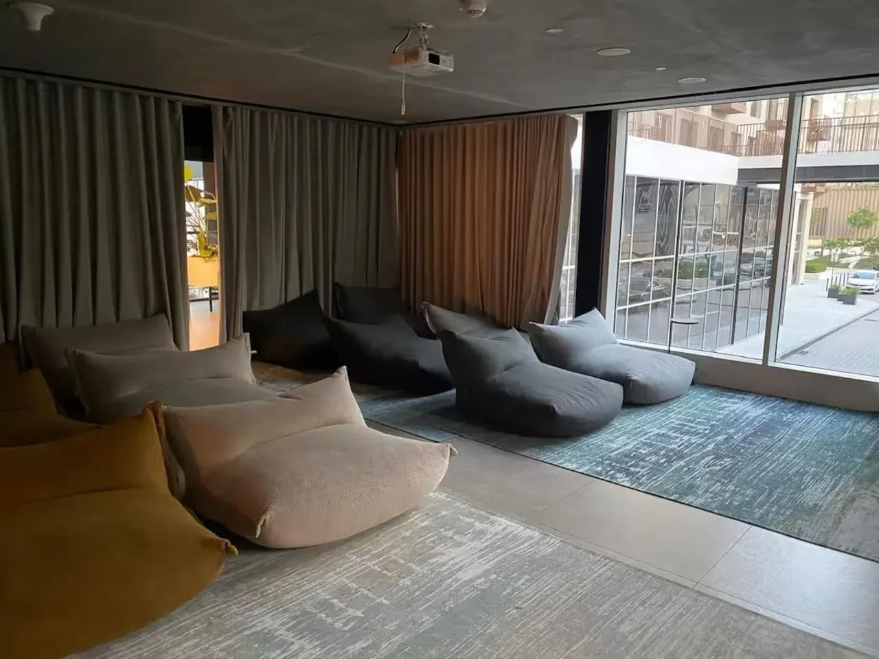A lounge area with low cushioned seating beside large windows.
