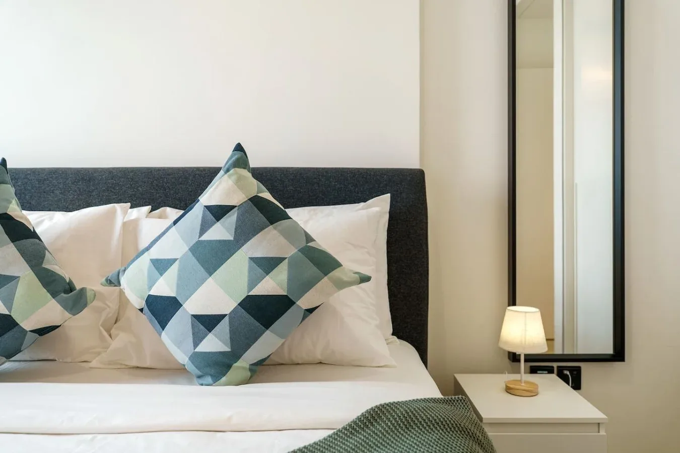 A bedroom with a neatly made bed and geometric patterned pillows.