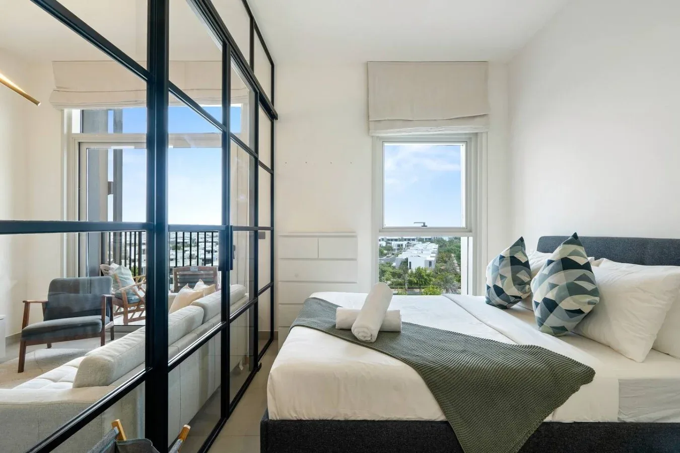 A bright bedroom with a bed beside a black-framed glass partition.