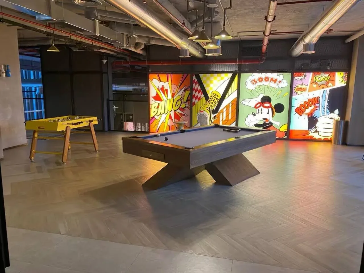 A recreation room with a pool table, foosball table, and colorful comic-style wall panels.