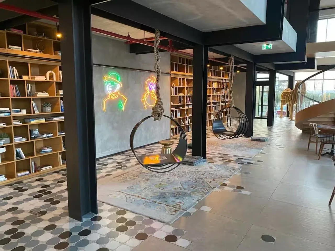 A modern lounge with hanging seats, bookshelves, and colorful neon wall art.