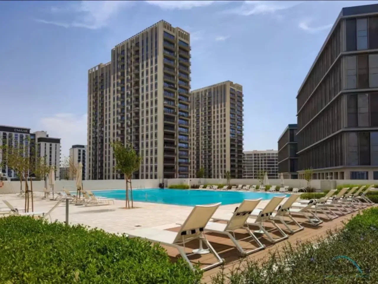 An outdoor swimming pool is surrounded by lounge chairs and tall apartment buildings.