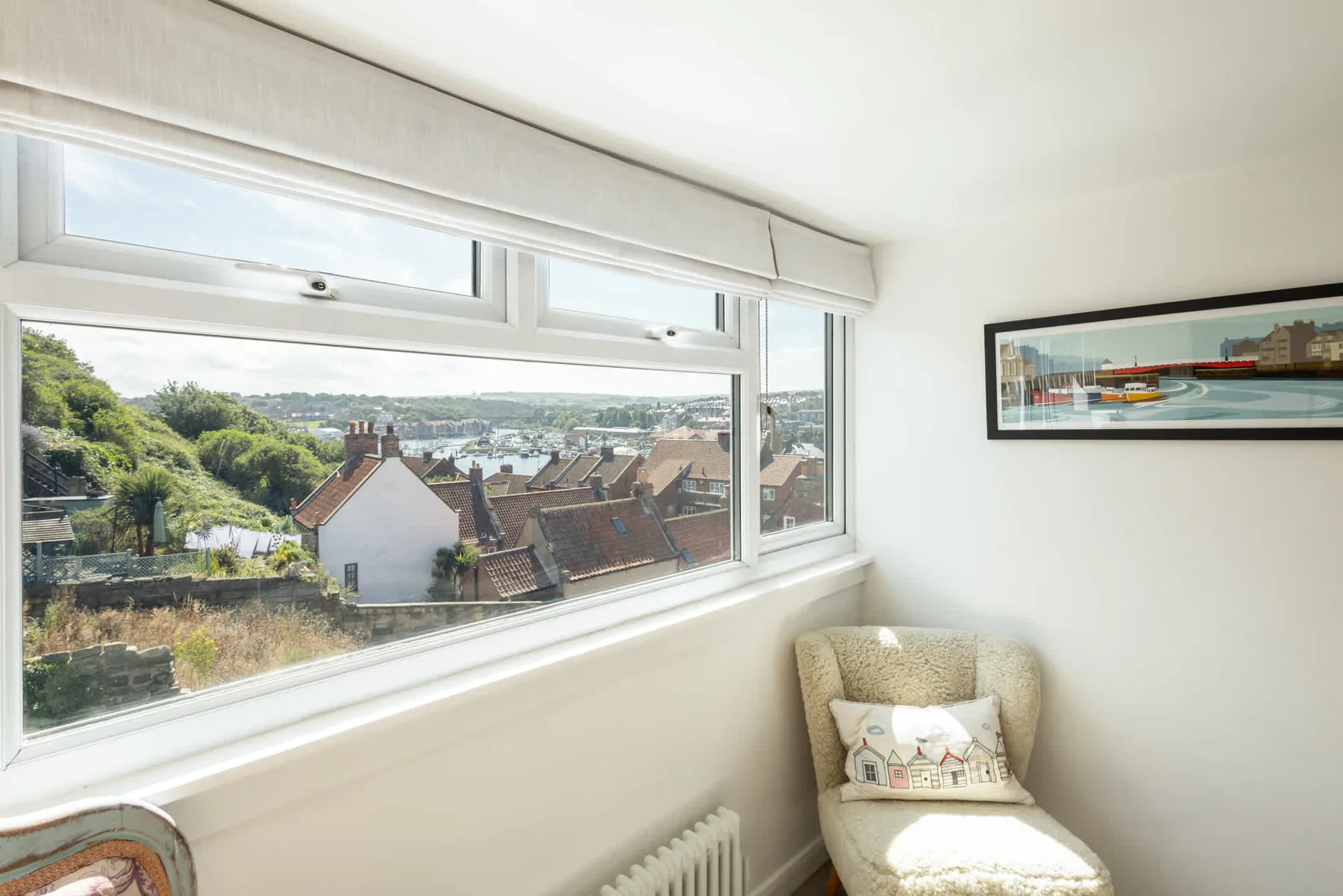 A bright sitting area has a large window overlooking rooftops and greenery.
