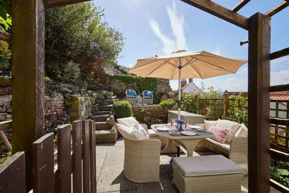 An outdoor patio has wicker seating and a large beige umbrella.