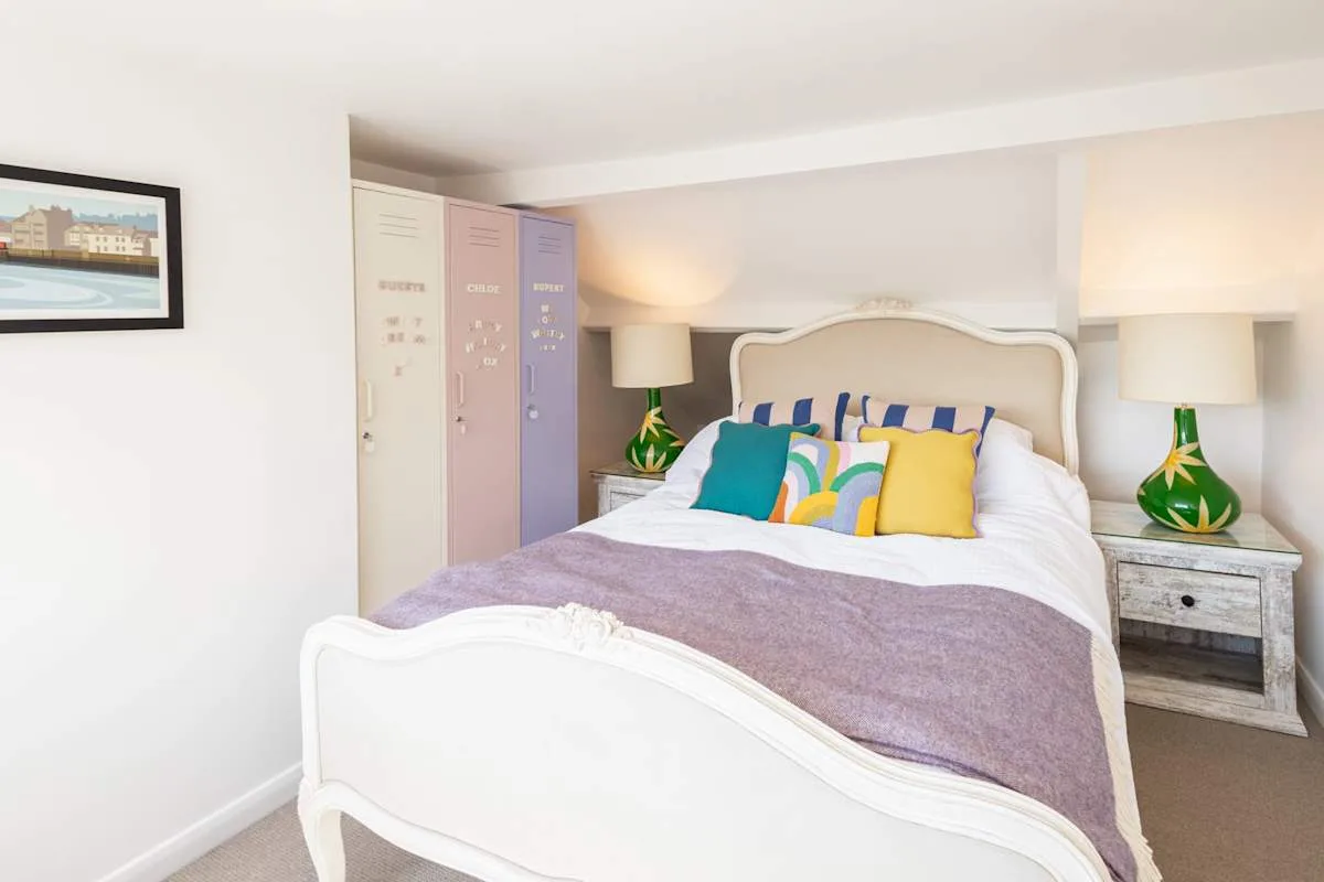 A bedroom with a white bed, colorful pillows, and matching bedside lamps.