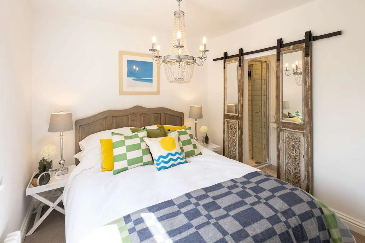 A bedroom with a neatly made bed, colorful pillows, and a hanging chandelier.