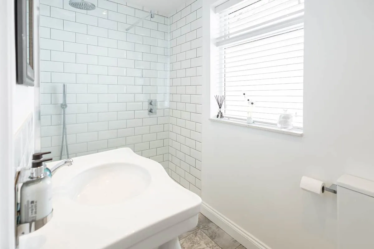 A bright bathroom with a tiled shower and a sink beneath a window.