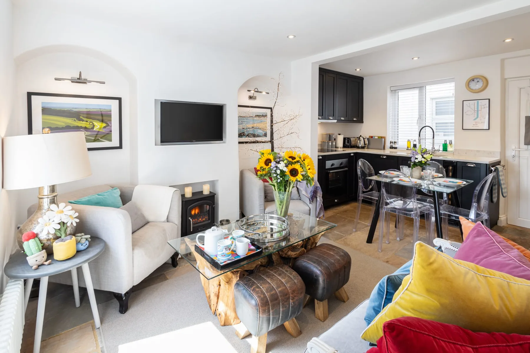 A living area with seating and a glass coffee table opens onto a kitchen and dining space.