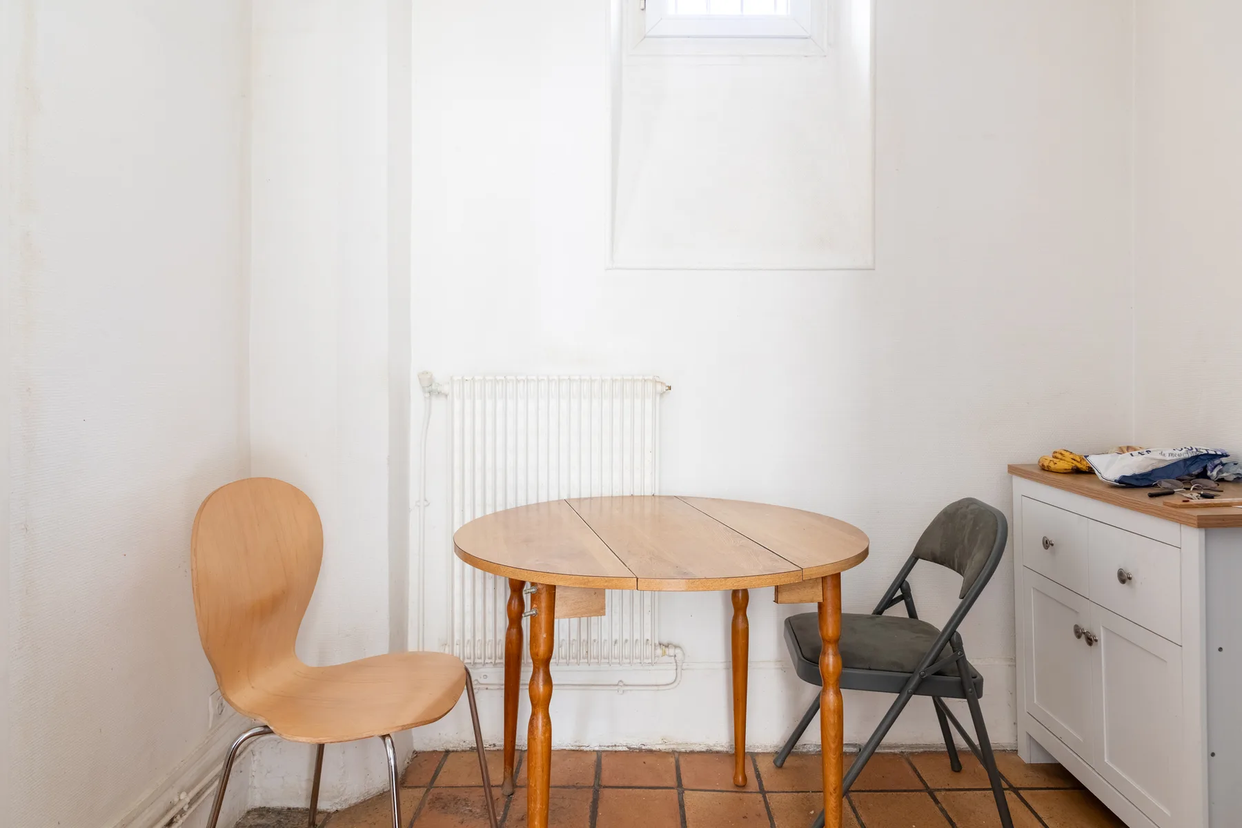 Una habitación luminosa con una mesa redonda de madera, sillas y una cómoda blanca.