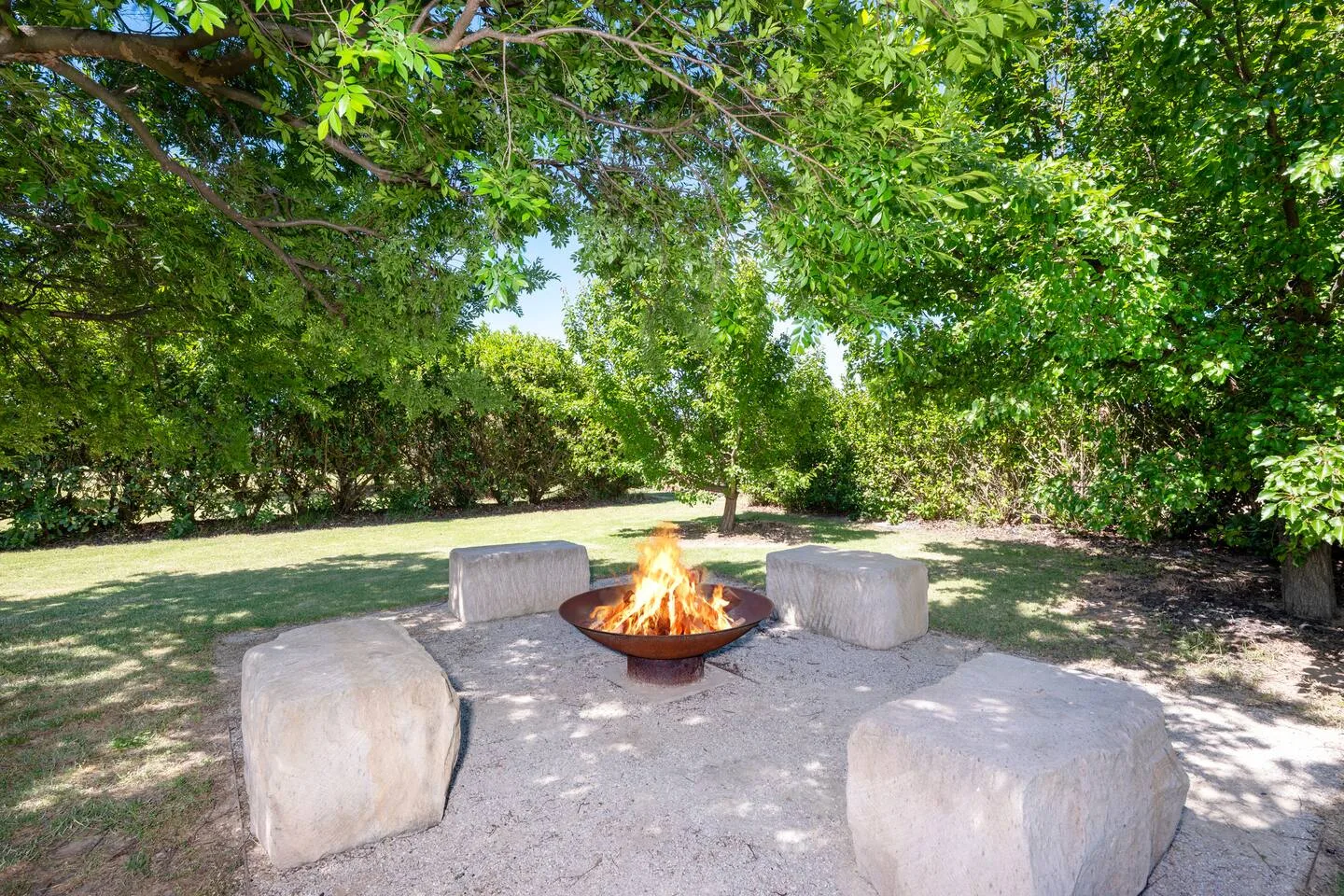 An outdoor fire pit sits among block seating in a tree-shaded yard.