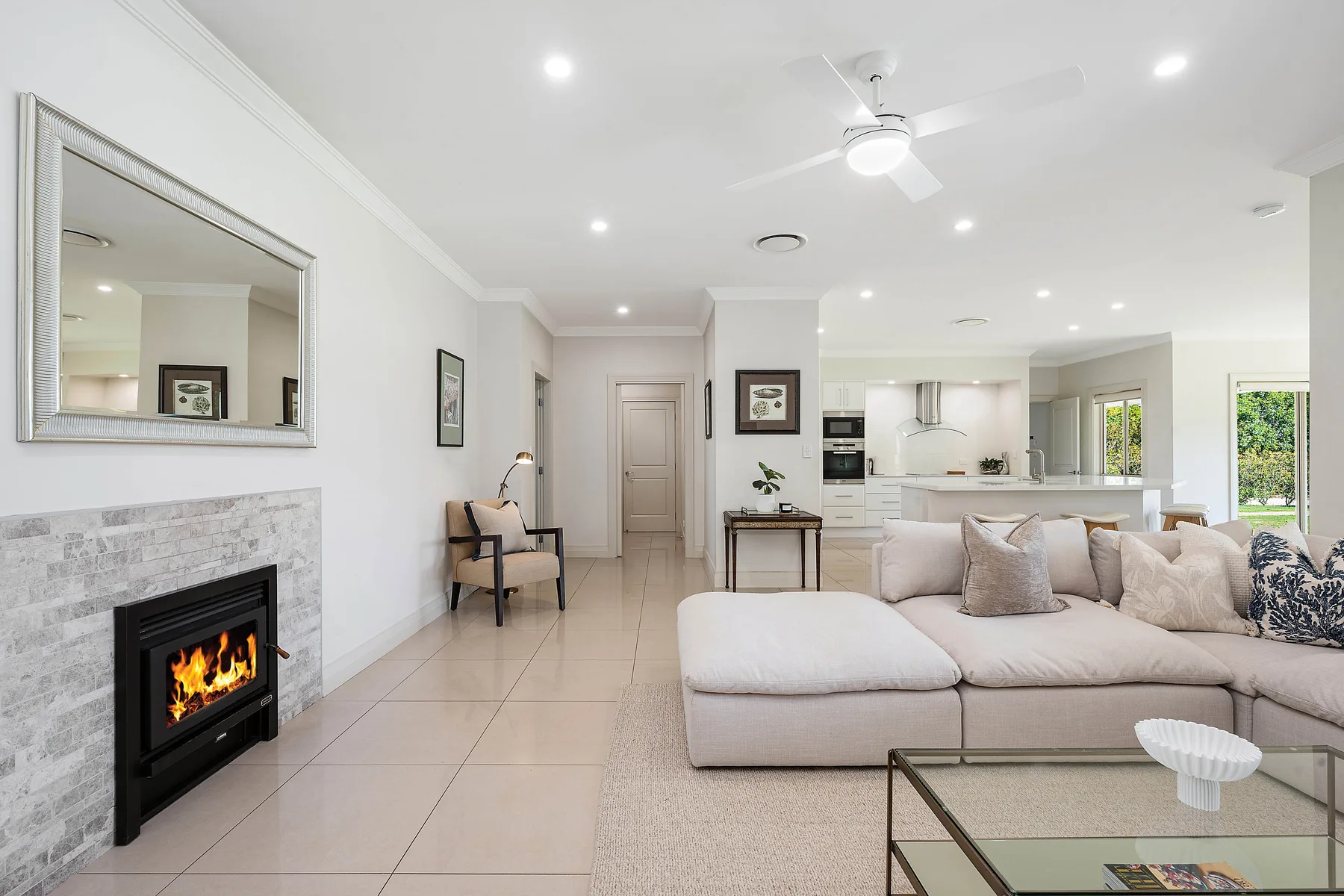An open-plan living room with seating, a fireplace, and a kitchen in the background.