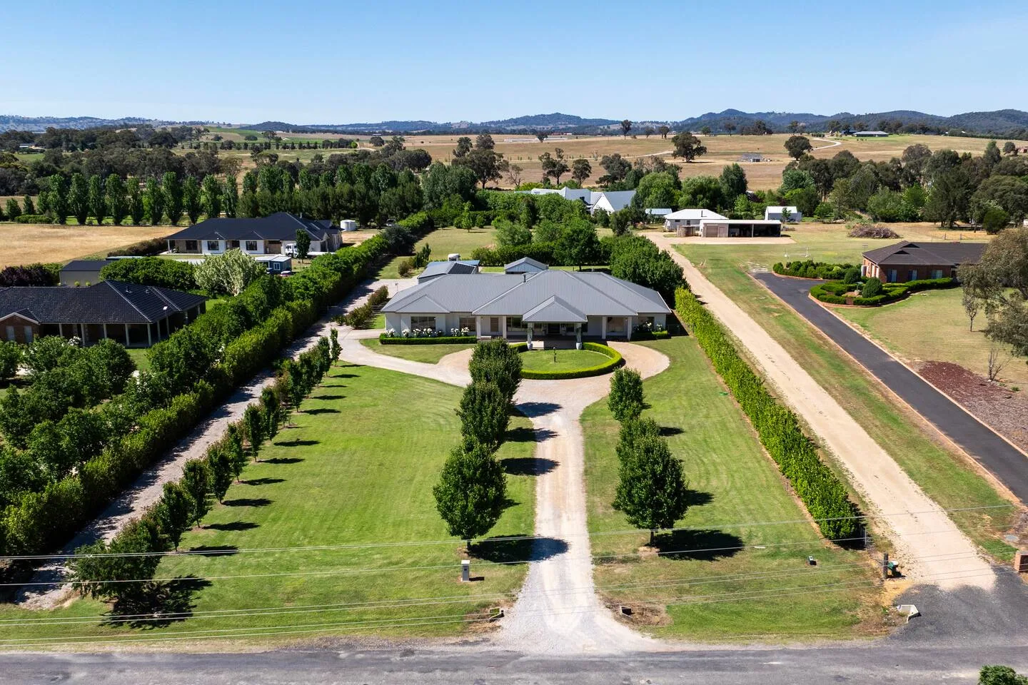 An aerial view shows a country property with a long driveway and landscaped grounds.