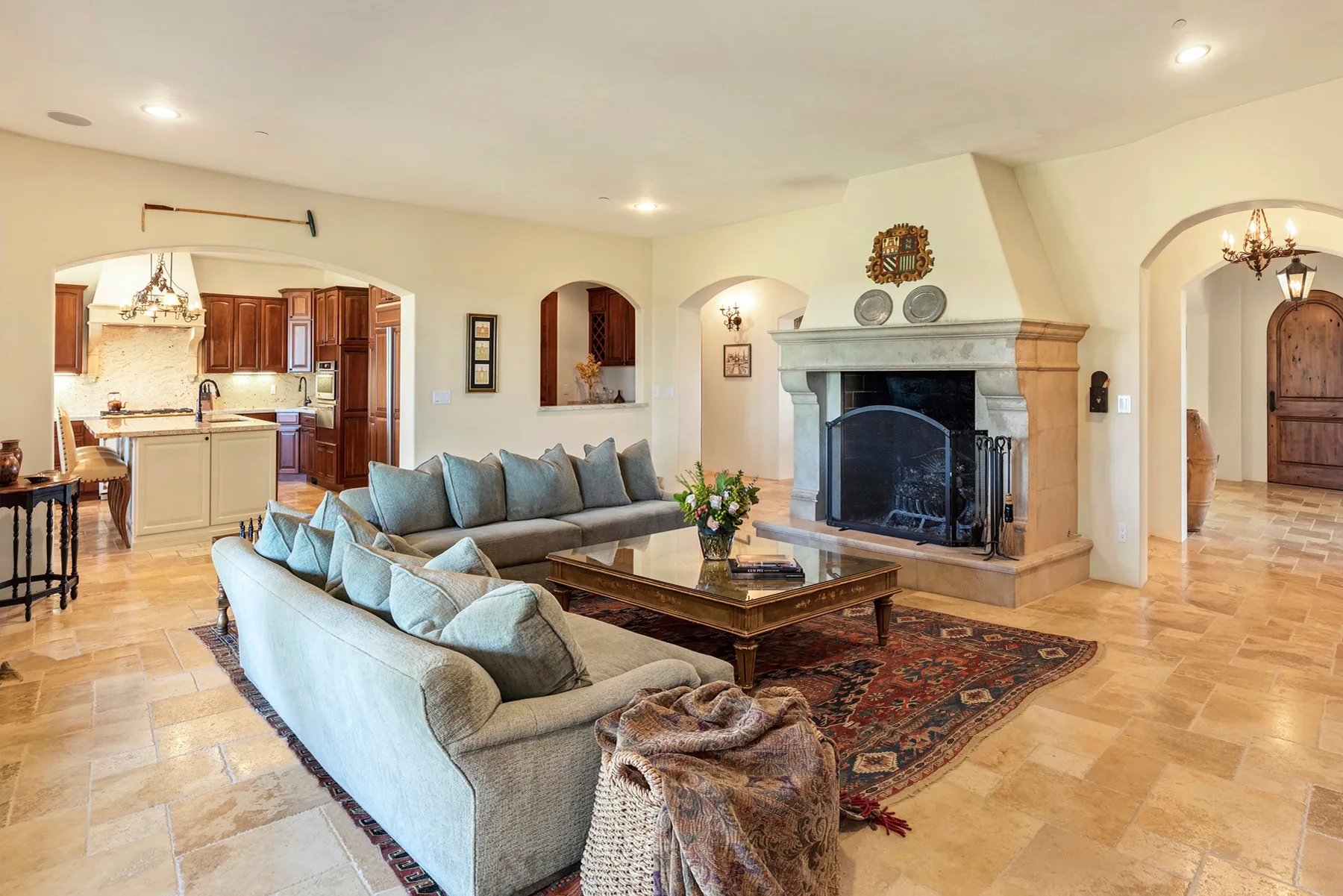 A spacious living room with seating around a fireplace and a view into the kitchen.