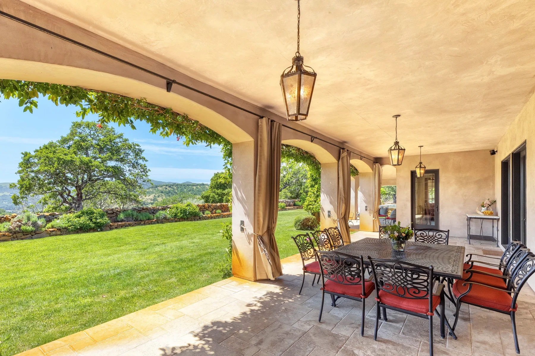 A covered outdoor dining area opens onto a green lawn and garden.