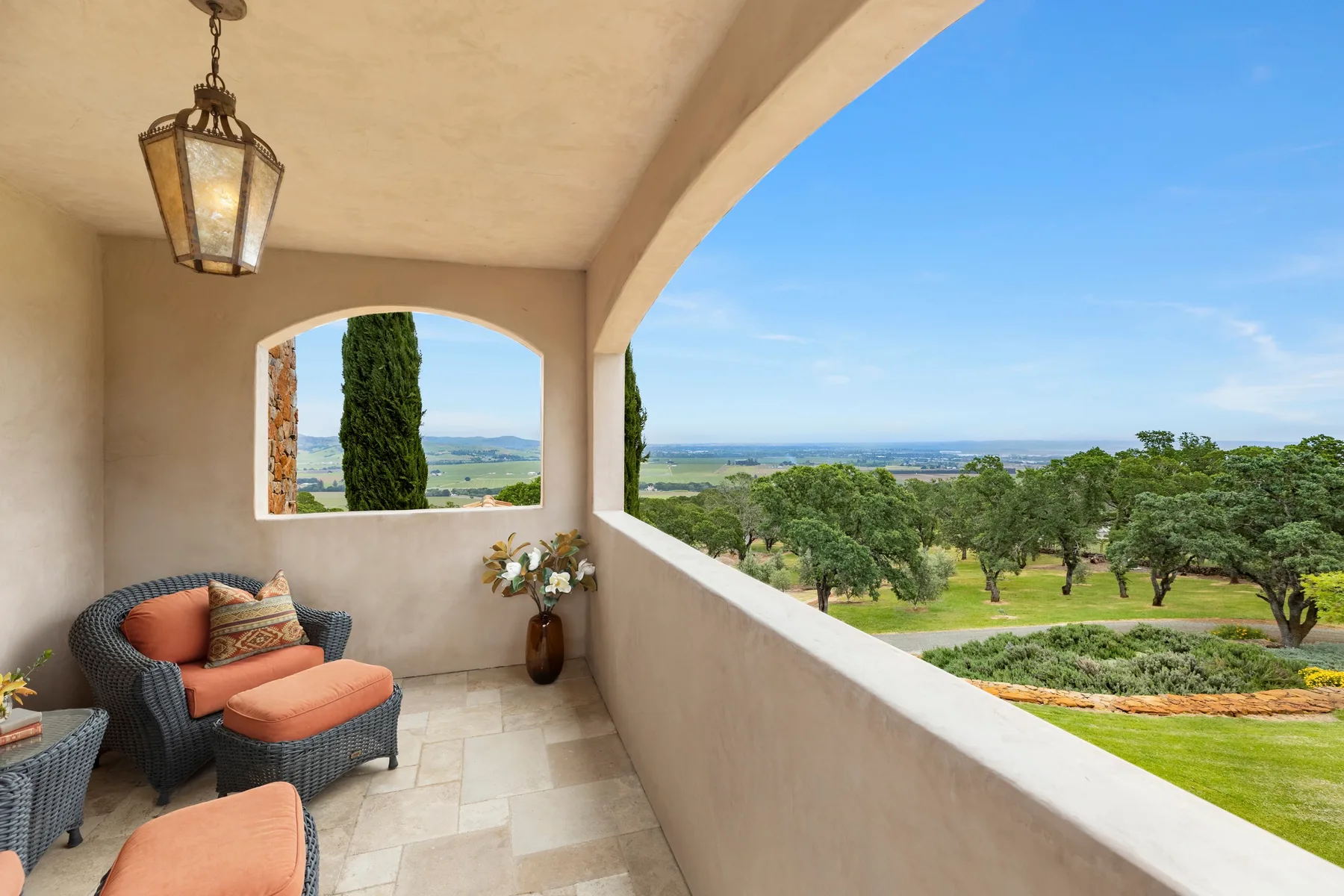 A covered balcony with cushioned seating overlooks green grounds and distant hills.