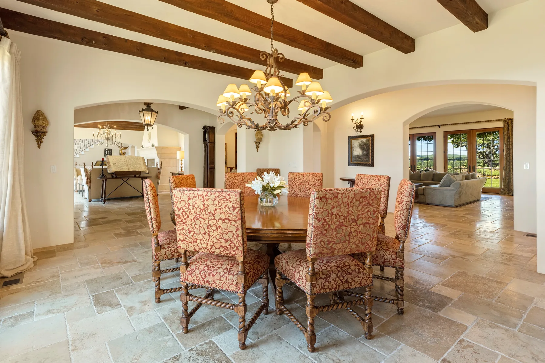 A dining area with patterned seating around a wooden table beneath a chandelier.